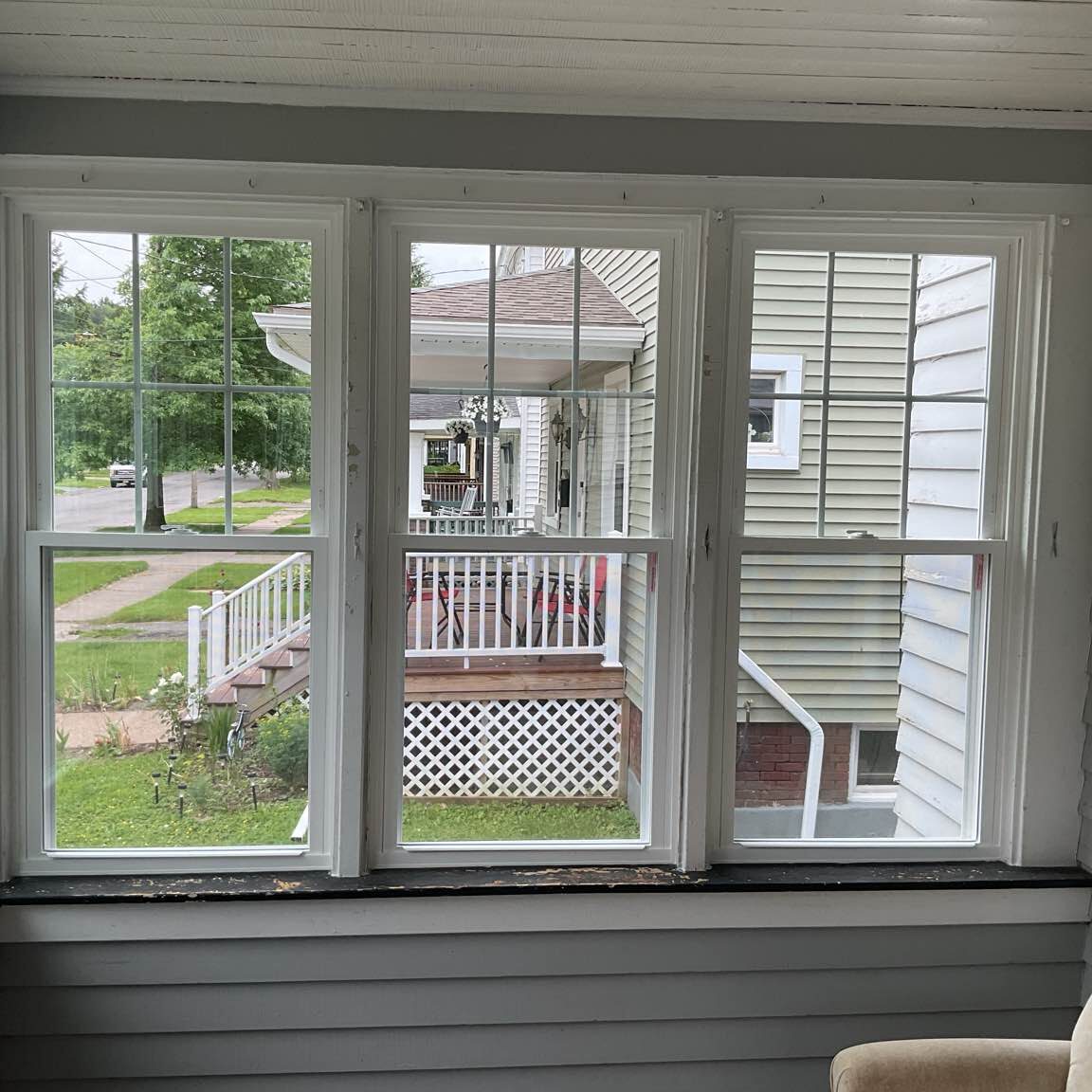 "Newly installed white double-hung windows with grids on a traditional home exterior, showcasing both sashes opened for ventilation.